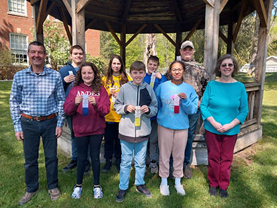 Science fair winners pose for a photo by a wooden gazebo, with ribbons in hand.